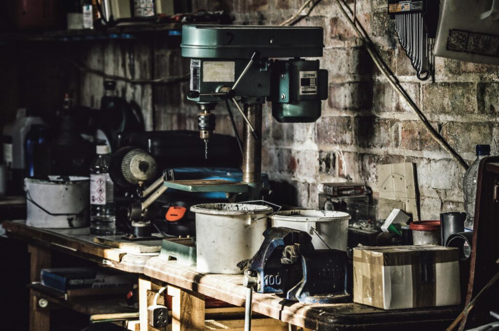 A detailed view of a cluttered workshop with a focus on a drill press and various tools.