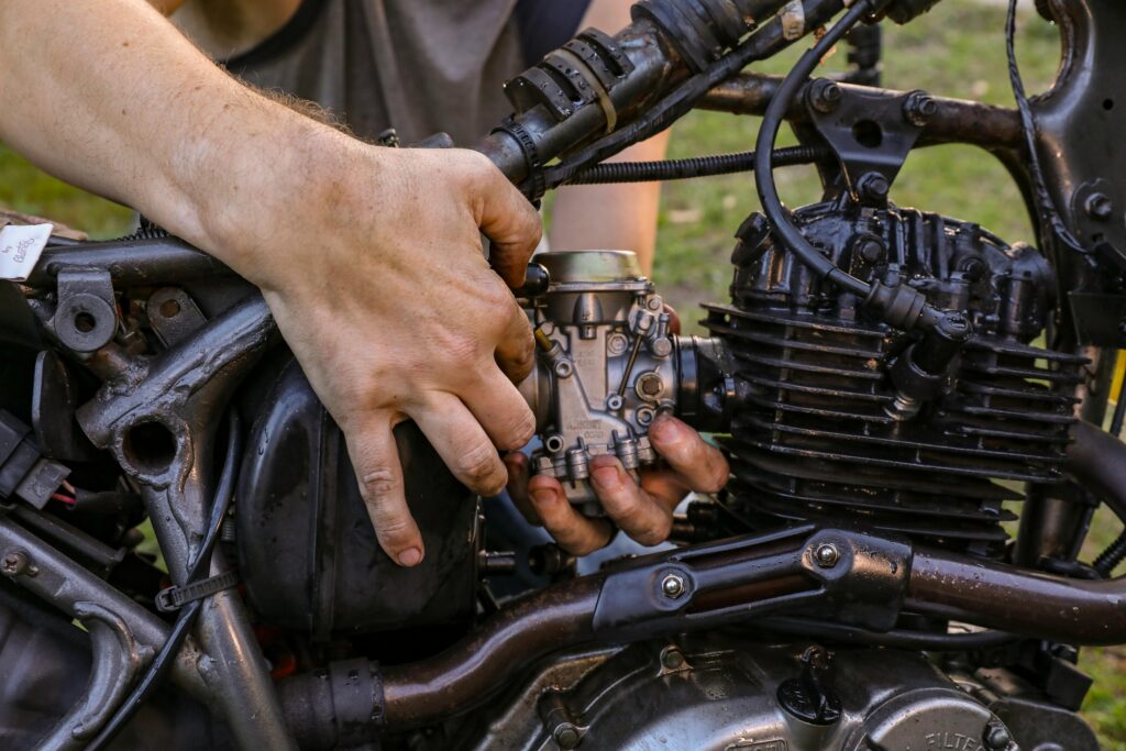 Close-up of a mechanic's hands fixing a motorcycle engine outdoors, showcasing expertise in engine repair.